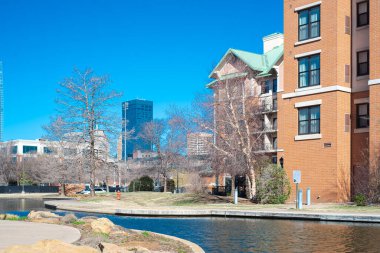 Hotels, buildings along Bricktown canal with downtown Oklahoma City skyline background, riverside restaurants, tourist attractions in Entertainment District, travel destination, water taxi. USA clipart