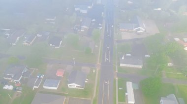 Foggy and misty morning light cover row of suburban houses near Gentry Avenue outside historic downtown of Checotah city in McIntosh County, Oklahoma lush green trees, aerial view small town. USA clipart