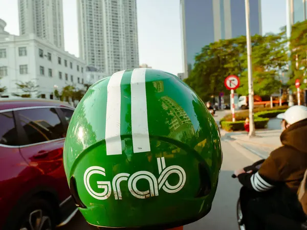 Stock image DEC 22, 2023-HANOI, VN: Office buildings along busy Ha Noi street with close-up view helmet Grab ride sharing driver using motorbike, Grab is Southeast Asia leading superapp, Singapore-based company