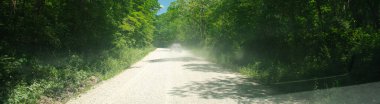 Panorama view car windshield view of dust gravel road in countryside of Mansfield, Missouri, rural path surrounding lush greenery tree canopy sunny blue sky, off-road remote area, back country. USA clipart