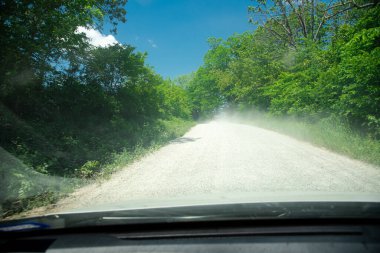 Mansfield, Missouri 'nin kırsal kesimindeki toz fırtınası yolunun ön cam manzarası yemyeşil ağaçların çevresindeki kırsal yol güneşli mavi gökyüzü, off-road uzak bölgesi, arka ülke, ulaşım. ABD