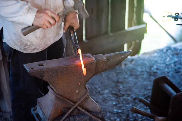 stock image Close-up blacksmith man hand using long carbon steel tongs with steel rivets and hammer to forge cast iron horseshoes melting on medieval anvil at traditional trade workshop, Mansfield, Missouri. USA