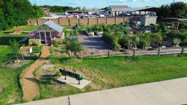 Kuzey Dallas 'ta büyük fabrika yakınlarında cam serası olan şehir bahçesi ahşap metal döşekler yükseltilmiş yataklar, depolama kulübeleri, Texas' ta bahçıvanlık yapan bir grup yama, anten. ABD