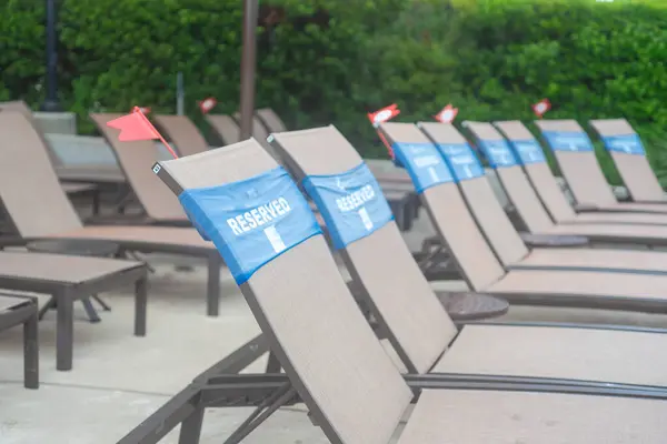 stock image Row of pool lounge chairs with reserved words wrap around and small plastic service flag at upscale hotel resort swimming in Grapevine, Texas, exclusive private seatings, summer holiday event. USA