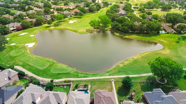 stock image Concrete titles and roof shingles of new development two story large mansion houses in upscale residential golf course community with sand trap bunkers, idyllic pond, Plano Texas, aerial view. USA