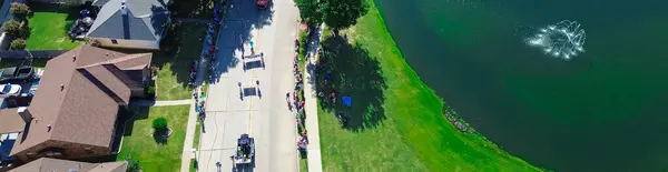 stock image Panorama aerial view pond water fountain along city street with large group of people and car parade to celebrate Independence Day Fourth of July in Coppell, Texas, traditional community event. USA