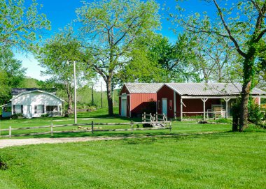Mansfield Missouri 'deki büyük bir arazideki kırmızı ahır çiftlik evi çimenli çimenler ve yemyeşil ağaçlar, tarım kasabasındaki huzurlu tarım kasabası kırsal tarım çiftliği. ABD