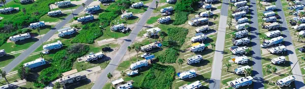 stock image Panorama aerial view large RV park campsite with long row of recreational vehicles, trailers boats and tall palm trees in South Padre Island beach, modern basecamp with full power hookup, Texas. USA