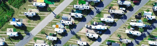 stock image Panorama aerial view large RV park campsite with long row of recreational vehicles, trailers boats and tall palm trees in South Padre Island beach, modern basecamp with full power hookup, Texas. USA