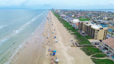 Aerial view multistory beach hotels, resorts, condos along sandy shoreline of South Beach with diverse people enjoy swimming, surfing, fishing, sunbathing, colorful umbrella tent, turquoise water. USA clipart