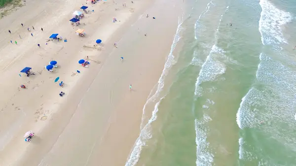 stock image Dense of beach umbrella, tent, camping and lounge chairs, diverse people family enjoy swimming, surfing, relaxing with emerald water calm waves at South Beach of Padre Island, Texas, aerial view. USA