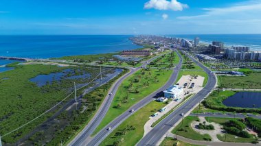 South Padre Adası kıyı lagünlerindeki Laguna Madre kıyısındaki State Park Road 100, körfez kıyısındaki kasaba bariyeri, yüksek katlı evler, sahil manzaralı oteller, turkuaz su, anten. ABD