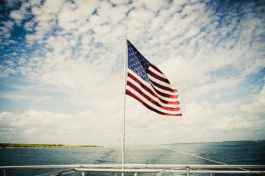 Gururla Amerikan bayrak direği okyanus teknesinde tur yunusu Güney Padre Adası, Teksas, Port Isabel arka planda, güneşli mavi gökyüzü, Bağımsızlık Günü vatanseverlik teması kırmızı mavi beyaz. ABD