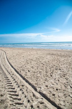 Güney Padre Adası 'nın beyaz kumlu kıyı şeridi boyunca ıssız bir plajda ATV izleri, Teksas' ın tropik plajı, güneşli mavi bulutlu gökyüzü, Körfez Kıyısı bariyerinde seyahat ve tatil yeri. ABD