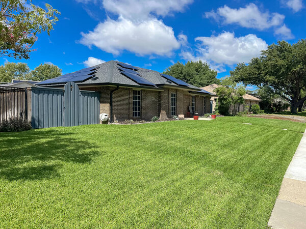 Concrete sidewalk pathway in front of single-family house with solar roof, grassy lawn sunny cloud blue sky in Coppell, suburb Dallas Fort Worth metroplex, green energy zero emission neighborhood. USA