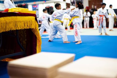 Tekvando kemeri tanıtım masası testlerinde geleneksel Kore nişanı ahşap kırma tahtaları, bulanık öğretmen, arka planda dövüş sanatları yapan üniformalı öğrenciler. ABD