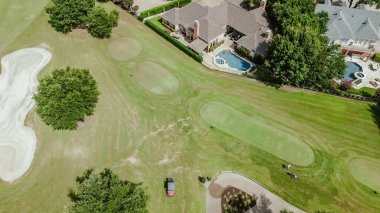 Upscale two-story suburban houses with swimming pools in golf course community in Plano, Texas, grassy country club with sand trap bunkers depression, club cars and golfers playing, aerial. USA clipart