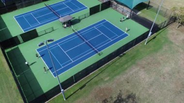 Spor giyimli bir grup bayan, Dallas Texas 'ın aydınlık kortlarında tenis dersleri alıyor. Gölgeli izleyici alanları, rahat bankları, top makineleri, üstgeçitleri olan, iyi ışıklandırılmış sert kortlar.