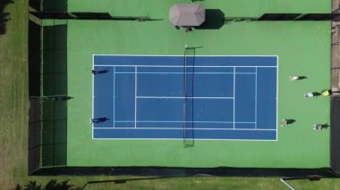 Dallas Texas 'ta oyuncularla, koçla ve makineli topla modern tenis kortunda, iyi aydınlatılmış sert kortlar grup dersleri, gölgeli seyirci bankları, üstgeçit.