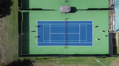 Spor giyimli bayanlar tenis grubu dersinde koç ve makine topu ile ışıklı saha sporu kompleksi Dallas Texas 'ta gölgeli izleyicilerin olduğu iyi ışıklandırılmış sert kortlar, rahat banklar.