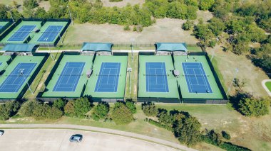 Lighted tennis court in sport complex outside Dallas Texas, well-lit hard courts with player practicing group lessons, shaded spectator areas and comfortable court benches, ball machine, aerial. USA clipart