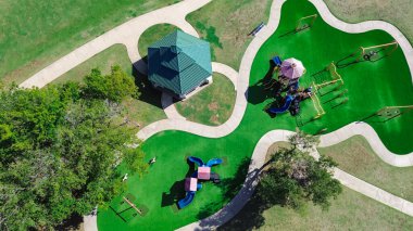 Yapay çimenlikli oyun alanı, pavyon ve tırmanma, Dallas 'taki açık hava eğlence tesisinde kaygan yapı, yapıda gölgeli çocuklar, beton patika, hava yolu. Teksas