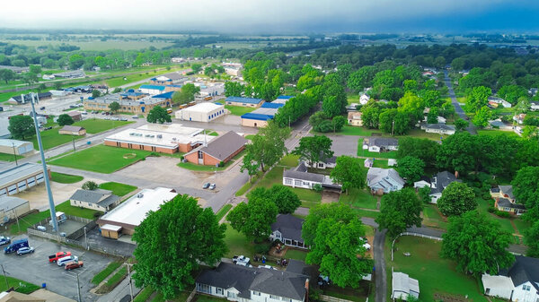 Traditional red brick buildings, residential houses in historic small-town USA of Checotah, McIntosh County, Oklahoma, churches, schools, large houses with vacant land, lush green trees, aerial. USA