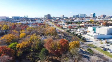 Yellow red orange fall foliage over urban park along Belt Line Road with office buildings, skylines, commercial complex in North Dallas and Addison, sunny clear blue sky, vibrant autumn leaves. USA clipart