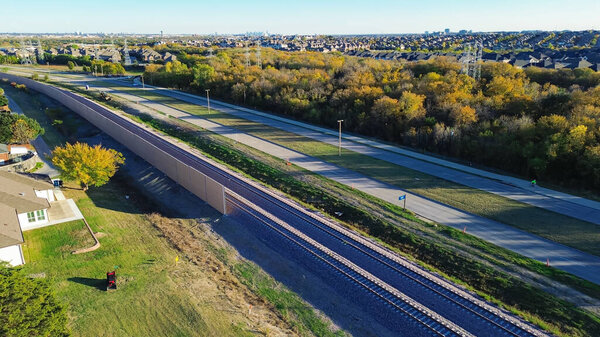 Belt Line Road with light railroad and precast concrete walls noise barrier, sound mitigation in upscale residential neighborhood downtown Dallas in background, absorptive acoustic in quiet zones. USA