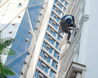 Hanoi 'deki yüksek bina kulesinin dışındaki yükseklikleri temizleyen Asyalı endüstriyel tırmanış işçisinin görüntüsüne baktığımızda, dağcılık halat erişimi sağlar ve ulaşılması zor yerlerde görevlerini yerine getirir. Vietnam