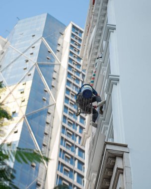 Hanoi 'deki ağaçlı yüksek bina kulesinin dışında yükseklik temizliği yapan Asyalı endüstriyel tırmanıcı, halat erişimi için zor yerlerde görev yapıyor. Vietnam