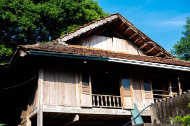 Geleneksel ahşap dikiş evinin üzerinde yosun bulunan eski kil kiremitler. Mai Chau köyü, Hoa Binh, Vietnam 'da açık pencere balkonlu balkon. Uzak bölgedeki Hindiçin kasabasının güneşli mavi gökyüzü. Asya