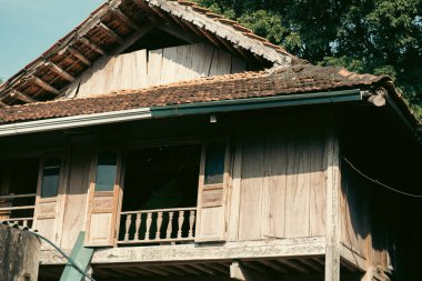 Geleneksel ahşap dikiş evinin üzerinde yosun bulunan eski kil kiremitler. Mai Chau köyü, Hoa Binh, Vietnam 'da açık pencere balkonlu balkon. Uzak bölgedeki Hindiçin kasabasının güneşli mavi gökyüzü. Asya