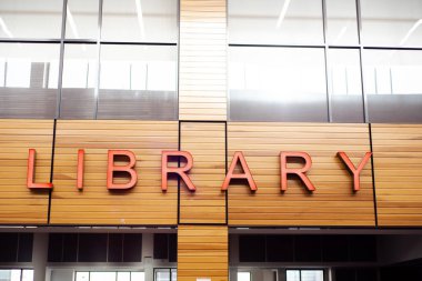 Dallas, Teksas 'taki ortaokul binasının girişindeki LED Kütüphane tabelasına yakın plan, iç kaplama duvarlı arka panelleri, cam pencereleri olan modern dış tasarım. ABD