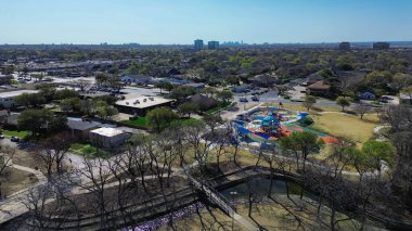 Dallas şehir merkezindeki parkın arka planında renkli bir oyun alanı, salıncaklar, engelli parklar, duyusal oyun alanı, patika, Rawhide deresi, Farmers Branch, Texas. ABD