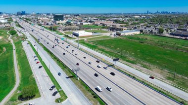 Arka planda Houston siluetleri bulunan Westchase iş bölgesindeki Sam Houston Tollway, çeşitli araçlar arasında yarı kamyonlar, arabalar, otoyoldaki karavan, gelişmek için büyük boş arazi yer alıyor. ABD