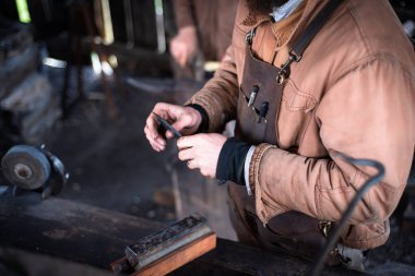 Mansfield, Missouri 'deki otantik ticaret atölyesinde Blacksmith' in deri önlükle yaptığı bıçak keskin testi, üst görünüm bileme taşı ya da bilenme taşı, demir çubuk metal işlerinde çelik aletlerin kenarları. ABD