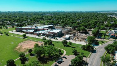 Kuzeybatı Dallas 'taki yemyeşil yemyeşil bölgede beyzbol parkı ilkokul yenileme şantiyesi şehir merkezindeki siluet arka planı Marcus Park, Dennis Rd yakınlarındaki konut binaları. ABD