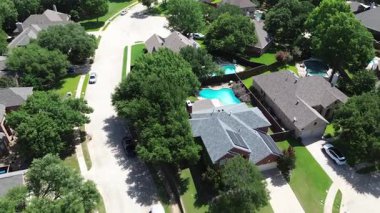 Lush green residential street with row of large modern suburban two-story homes well-maintained green lawns, solar roof panels and driveway parking on a sunny summer day, Flower Mound, Texas