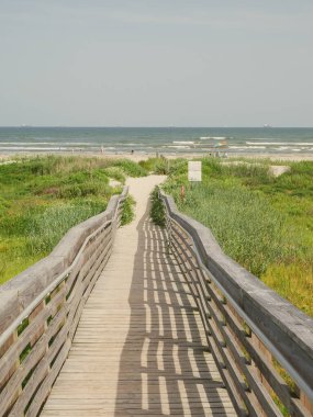 Uzun tahta kaldırım insanların dinlendiği Galveston plajına çıkar, gökkuşağı renkli şemsiye. Kıyı otları, okyanus dalgaları ve güneşli gökyüzü boş zamanları, doğayı, körfez sahili aktivitelerini ön plana çıkarıyor. ABD