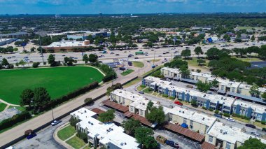 Kentsel alçak katlı düz çatılı apartman kompleksi binalar, yeşil alan ve ABD-75 otoyolu boyunca işlek perakende ve iş koridoru, yoğun trafik ve ticari mülkler görülebilir. ABD