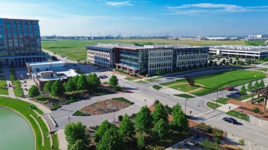 Sculpture plaza at business district in Cypress Waters, Dallas with glass office buildings, rooftop HVAC units, multilevel garage with canopy, curved pond trails, urban planning corporate design. USA