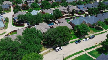 Tree-lined residential street in Coppell, Texas with parked cars, two-story homes, fenced backyards, private pools, rear alley garages in quiet, HOA-managed suburban neighborhood, suburbs Dallas. USA