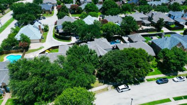 Tree-lined residential street in Coppell, Texas with parked cars, two-story homes, fenced backyards, private pools, rear alley garages in quiet, HOA-managed suburban neighborhood, suburbs Dallas. USA