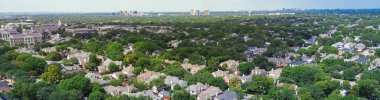 Panorama aerial view University Park showing US 75 busy traffic along upscale homes with sound barrier wall, mature trees, college campus with construction, skyline transition Dallas high-rises. USA