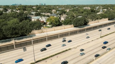 Midtown Dallas skyline background from dense traffic US 75 corridor highway with sound barrier wall separates expressway from upscale University Park residential homes, urban-suburban transition. USA