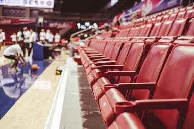 Motion blurred basketball player dribbles background from folded stadium chairs with cup holders line the court edge. Capturing quiet tension, readiness of youth game moment in Dallas, Texas. USA