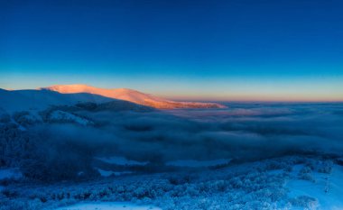 Bright orange dawn in the mountains. Trees are covered with snow and hoarfrost.