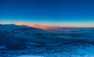 Bright orange dawn in the mountains. Trees are covered with snow and hoarfrost.