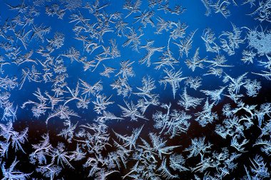 Frost on the glass. Abstract natural texture. Drawing of ice crystals on a blue background.